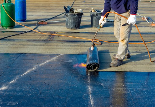 Worker preparing part of bitumen roofing felt roll for melting by gas heater torch flame Worker preparing part of bitumen roofing felt roll for melting by gas heater torch flame